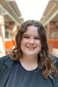 woman with wavy brown hair wearing a black shirt and black jacket standing in Spellmann Center